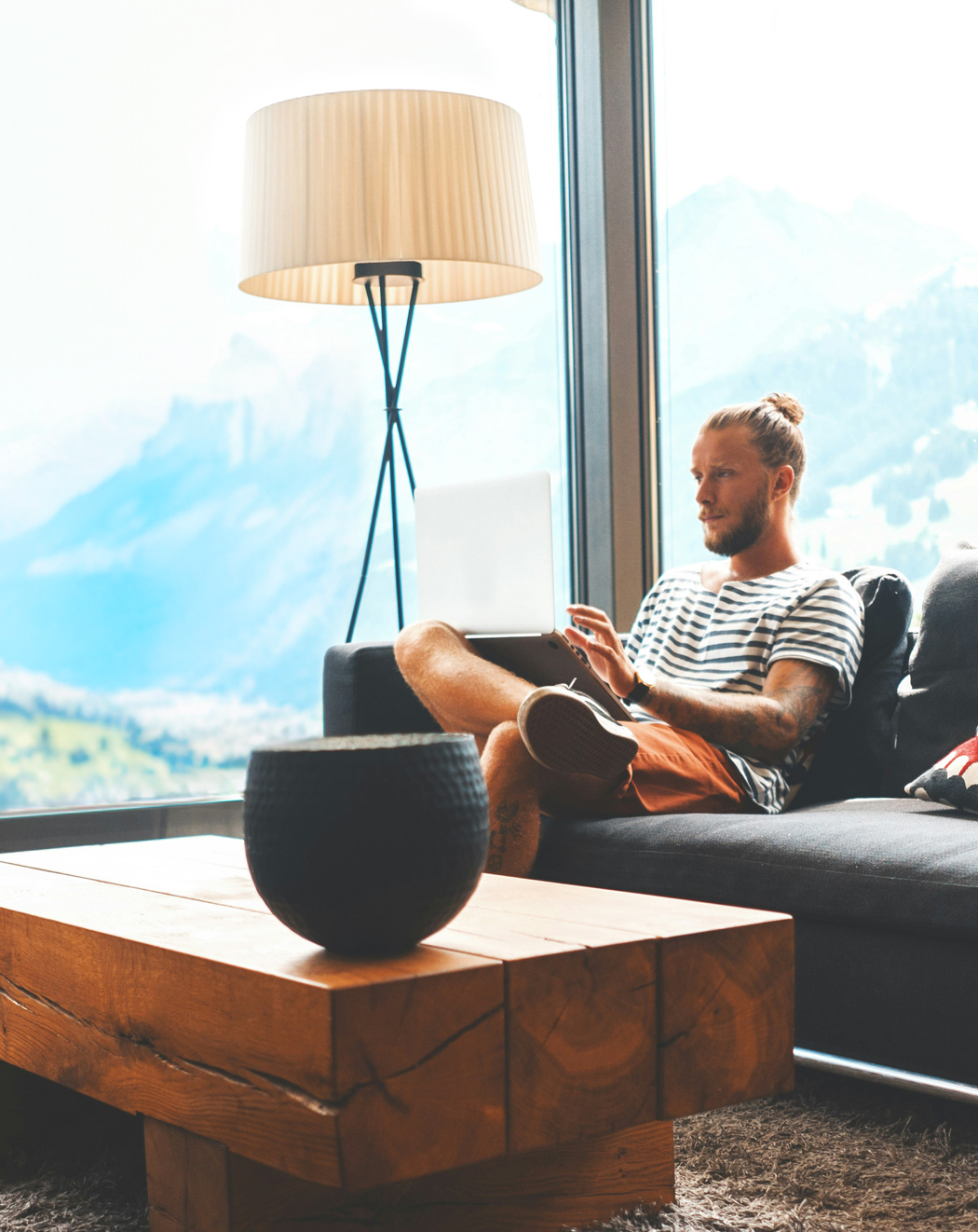 Vorschaubild Blogartikel Digitalinkasso in der Schweiz. Mann Mitte 30 sitzt auf einer Couch und hat einen Laptop auf dem Schoß. Im Hintergrund sieht man durch große Fenster die schweizer Berge.